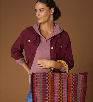 Woman model wearing maroon jacket with multicolored tote handbag.