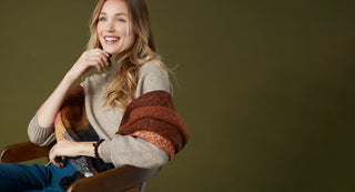 Model wearing tan sweater with multicolored autumn scarf. Shop fall/winter collection.