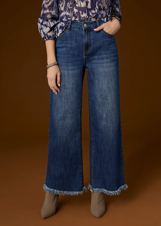 Model wearing blue denim wide leg jeans on brown background.