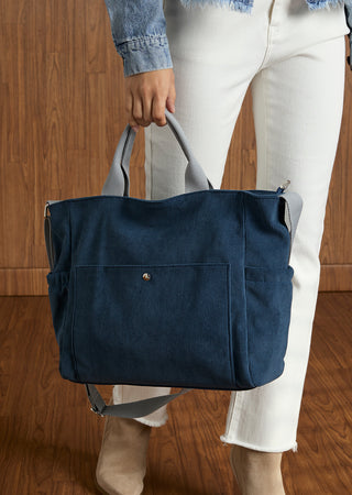 Model holding blue tote handbag on wood textured background.