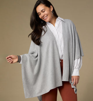 Woman wearing a gray poncho over a white shirt on a beige background