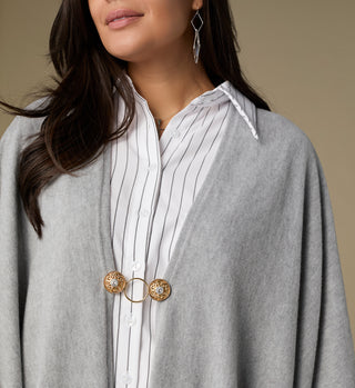 Woman wearing a gray cardigan over a white shirt with a gold brooch.