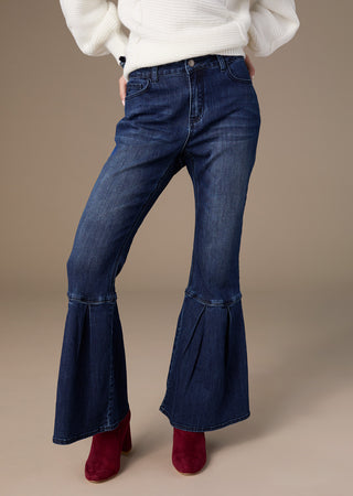Person wearing blue flared jeans and red shoes on a beige background
