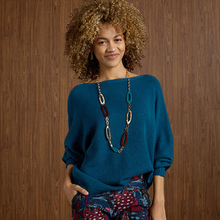 Woman wearing a blue sweater with a long necklace against a wooden background