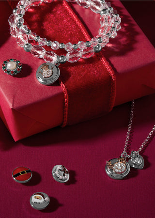 A jewelry set displayed on a red gift box and dark red fabric background, including a clear faceted beaded bracelet with a round silver pendant, a silver necklace with heart and oval pendants, a green-and-white brooch, and several small round pin-style accessories.