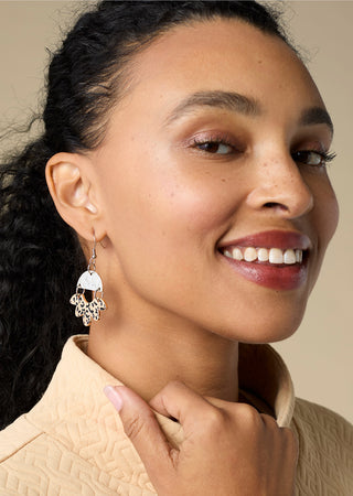 Model wearing dangle earrings on a tan background.