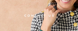 A close-up lifestyle shot of a woman wearing a black and white houndstooth jacket with gold buttons, touching her neck with a black beaded ring. The text 'CONTACT US' is overlaid in the center on a soft beige background.