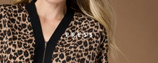 Close-up of a model wearing a leopard print jacket with black trim and a black zipper, featuring the brand name 'PRESS' overlaid on the chest.