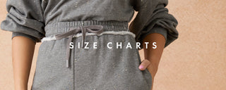 A cropped view of a person wearing a gray textured sweatshirt and matching pants, with the words 'SIZE CHARTS' overlaid across the center against a warm beige background.