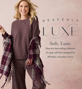 A smiling blonde woman models a soft knit lounge set in a dusty mauve-brown color, featuring a long-sleeve top and matching pants, with a matching plaid fringed throw draped over her arms. The background is a soft pink textured backdrop with text reading 'HEAVENLY LUXE Soft.