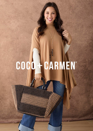 A woman models a tan asymmetrical poncho-style top with white long sleeves, paired with blue jeans and holding a woven tote bag. The brand name 'COCO + CARMEN' is displayed in white text across the center.