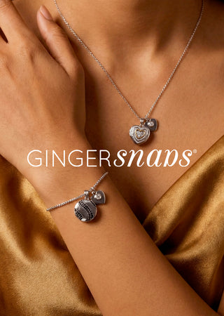 A close-up lifestyle shot of a model wearing a silver necklace and bracelet set from Ginger Snaps, featuring heart-shaped charms, set against a warm gold satin background.