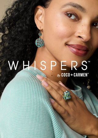 A close-up lifestyle shot of a woman wearing a matching turquoise and gold ring and earring, with her hand resting on her shoulder. The brand name 'WHISPERS by COCO + CARMEN' is displayed in white text across the center.