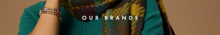 A close-up of a person wearing a teal knit top and a patterned scarf in teal, brown, and mustard tones, with stacked metallic bracelets on one wrist. White text across the center reads 'OUR BRANDS' on a warm beige background.