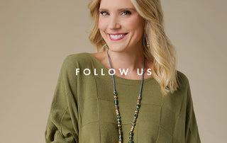 A smiling blonde woman wearing an olive green knit top and a long beaded necklace, photographed against a plain warm beige background with the text 'FOLLOW US' overlaid across the center.