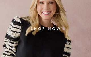 A smiling blonde woman wearing a black top with black-and-white patterned sleeves, posed against a soft pink background with the text 'SHOP NOW' overlaid across the center.