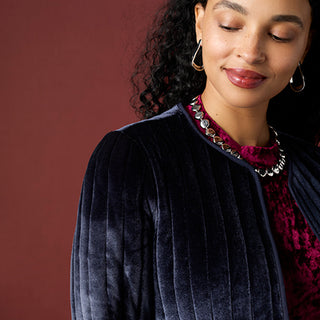 Model wearing blue jacket and red top on red background.