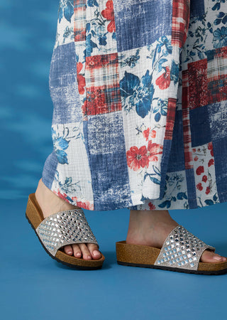 Silver sandals worn with a patchwork skirt against a blue background