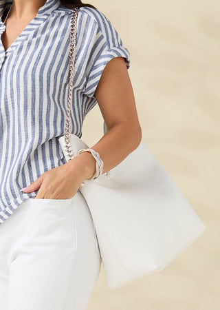 Person wearing a blue and white striped shirt with white pants on a beige background