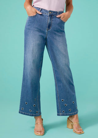 Person wearing blue jeans with heart details on a teal background