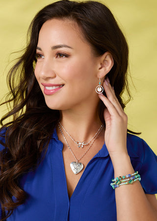 Woman wearing jewelry including earrings, necklaces, and a bracelet against a yellow background