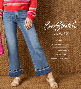 Model wearing dark denim jeans on a tan textured background promoting 'EVERSTRETCH' denim collection. 