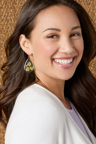 Model smiling wearing teardrop earrings on a tan textured background.