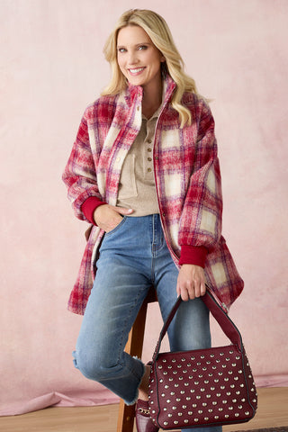 Model wearing a tan shirt with plaid jacket and denim on a light pink background.