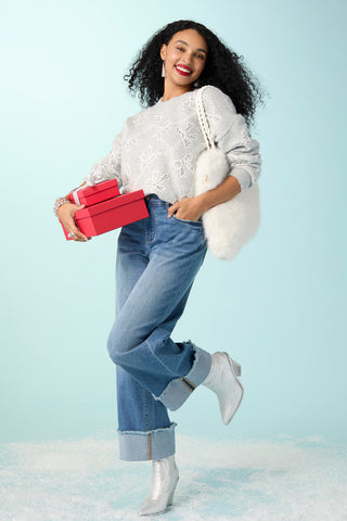 Model wearing white sweater with ribbon and blue jeans on a light blue background.
