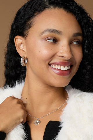Model wearing silver hoop earrings and silver necklace on a dark tan background.