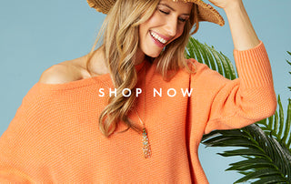 Model wearing a bright orange summer sweater, a necklace, and hat.