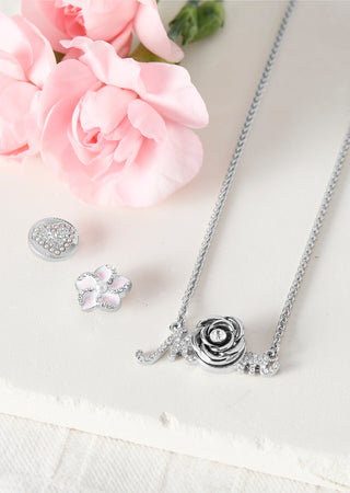 Silver necklace with rose design on a white surface with pink flowers