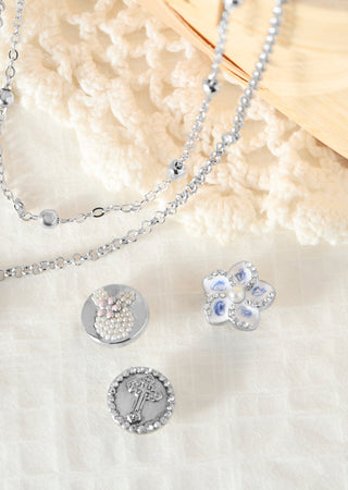 Silver jewelry set including a necklace and pendants on a textured surface.