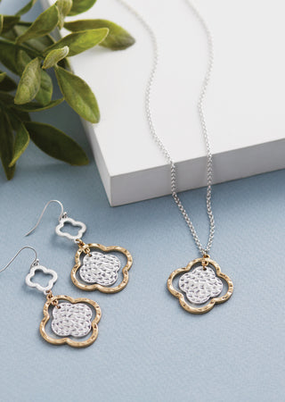 Jewelry set with necklace and earrings on a light blue surface with green leaves in the background