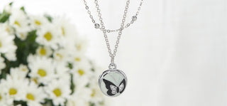 Silver necklace with a butterfly pendant in front of white flowers